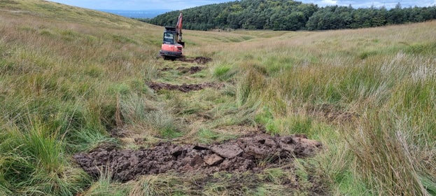 A digger surrounding by diagonal heaps of earth on the moorland at Lyme as part of the Riverlands deculvertering project